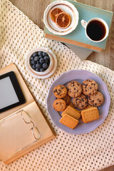 Plate of cookies, cup of tea, fresh blueberries, dry oranges, stack of books, reading glasses and tablet on the table. Hygge at home. Flat lay.
