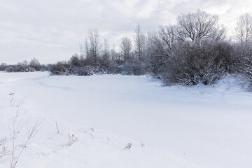 Rural winter landscape with snowy river bank and bare trees