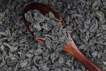 Green twisted tea leaves in a wooden spoon. Chinese tea is scattered on the table in large quantities. top view