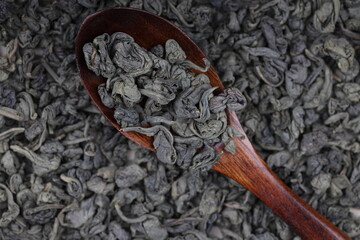 Green twisted tea leaves in a wooden spoon. Chinese tea is scattered on the table in large quantities. top view