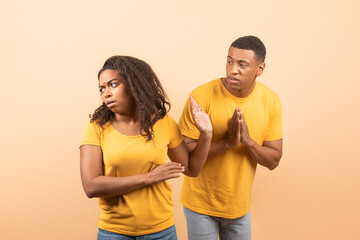 Black husband trying to talk and reconcile with offended wife, standing over yellow studio...
