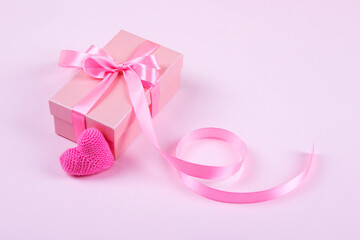 Happy Valentine's Day, Mother's Day and birthday greeting card. Knitted pink heart and gift box with a satin ribbon bow on a pink background