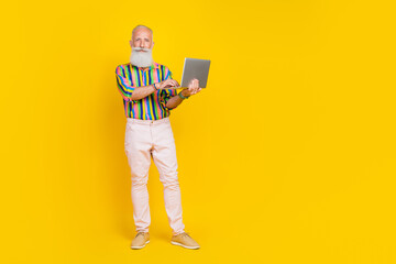 Full body portrait of calm serious aged man use wireless netbook empty space blank isolated on yellow color background