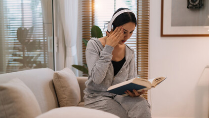 adult gorgeous woman reading book headache touching head wearing headphones. pretty woman hurt from...