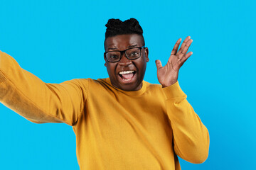 Naklejka premium Cheerful Black Young Man Wearing Eyeglasses Taking Selfie Over Blue Background