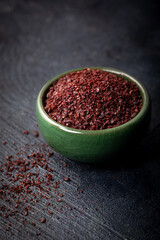 Dried ground red Sumac powder in a green bowl on dark background.