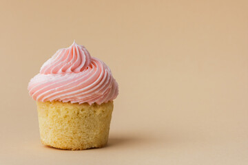 Close-up of vanilla cupcake with pink whipped butter cream top. Cream cheese frosting on muffin decorated with little pink heart shaped chocolate topping. Beige background. Happy Valentine's Day