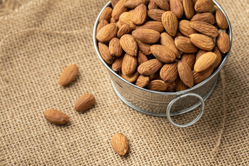 Metal bowl full of almonds on a sackcloth. Pile of nuts stacked together randomly on the burlap background. Healthy nutrition concept