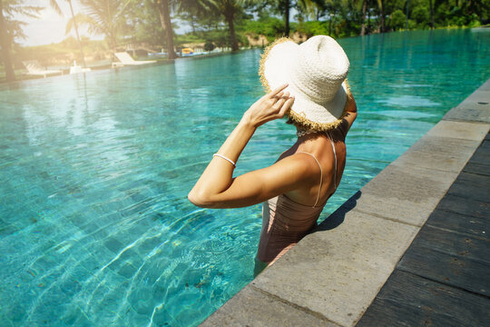 Photo of young woman wearing summer hat relaxing in big swimming pool with blue water on a sunny day. Copy space.
