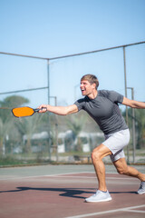 man playing pickleball game, hitting pickleball yellow ball with paddle, outdoor sport leisure...