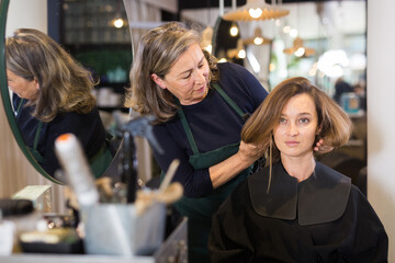 Elderly woman professional hair stylist discussing young female customer preferences in salon,...
