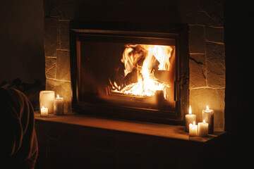 Cozy burning fireplace and candles in dark evening room. Fireplace heating in house, electricity...