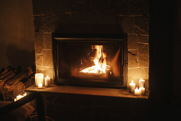 Cozy burning fireplace and candles in dark evening room. Fireplace heating in house, electricity...