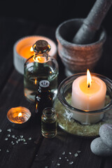 Spa setting with essential oil, candle, sea salt, pebbles, towel on dark wooden background. Massage, aromatherapy. Natural organic ingredients for relaxation, detention. Wellness in salon concept