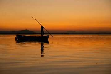 Fototapeta premium Sunset in Denizli Civril illuminated lake is approaching the shore with a fishing boat