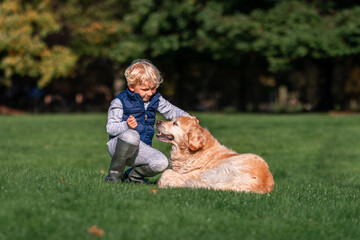 Little boy playing and training golden retriever dog in the field in summer day together. Cute child with doggy pet portrait at nature