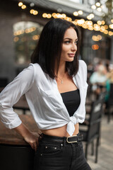 Fashionable beautiful woman in stylish casual clothes with a white shirt with a black top and jeans in the city