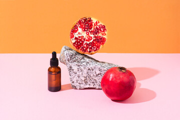 Natural cosmetic oil or pomegranate serum on natural stone. Balance composition, orange and pink background, eco friendly cosmetics, vitamin skin care, front view