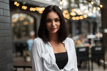 Urban female portrait of a beautiful stylish girl with a bob haircut in a stylish white shirt walking on the street with bokeh lights
