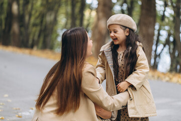 Fototapeta premium Portrait of happy mother and daughter spending time together in autumn park with falling yellow leaves