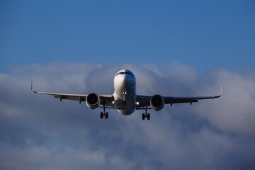 Landing plane on cloudy sky background, front view