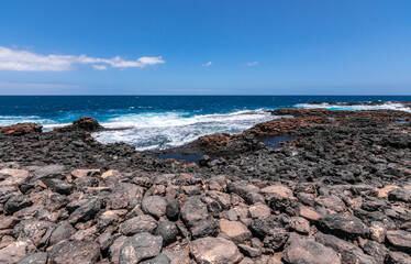 Fototapeta na wymiar Wild rocky coastline of Fuerteventura, Canary Islands, Spain. A big wave crashes on the rocks in rocky bay. Squirrels hiding among the rocks.