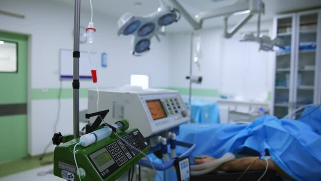 Modern medical equipment working in the surgery room during surgery. Diverse tubes from apparatuses connected to a patient lying on the surgical table.
