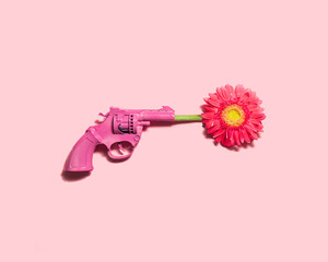 Pink flower and gun on pastel light pink background. Minimalistic love concept. Creative peace flat lay idea.