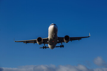 Landing plane on cloudy sky background, front view