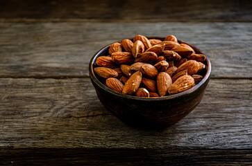 Almond nuts in earthenware on a wooden background.
