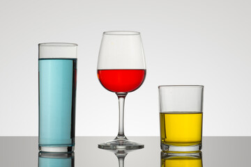 Minimalist composition of a glass and glasses on a glass base, with colored drinks