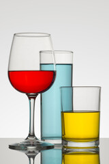 Vertical minimalist image of a glass and crystal glasses with colored drinks, and a white background
