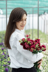 Businesswoman holds a beautiful bouquet in the green house. Woman portrait with flowers. Female florist has an order for fresh flowers.