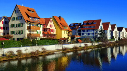Fototapeta na wymiar Wohnhäuser spiegeln sich im Wasser entlang des Neckars in Rottenburg unter blauem Himmel