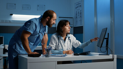 Clinical staff looking at computer monitor analyzing patient medical expertise while discussing...