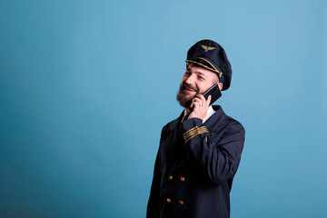 Middle aged captain talking on modern phone, holding smartphone, having conversation. Airlane aviator in uniform with calm neutral facial expression answering telephone call