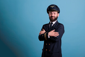 Airplane pilot wearing uniform and hat portrait, confident plane captain standing with crossed arms, looking at camera. Smiling civil aviator with badge on professional suit