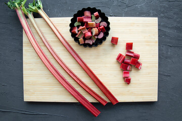 Fresh rhubarb on wooden cutting board on black background, top view. 