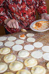 Unrecognizable aged woman filling dumplings with tuna, boiled egg and tomato sauce.