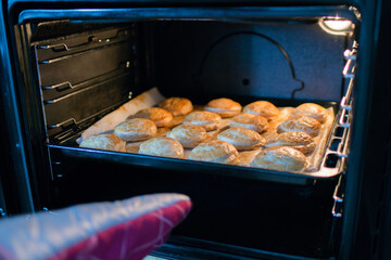 Human hand with an oven glove taking out of the oven a tray with pastry dumplings