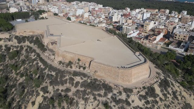 Bright, sunny aerial shot of the castle at Guardamar del Segura in Spain. Highlights the castle’s remains, the colorful architecture of the nearby town, and the blues of the ocean. Zoom in shot
