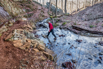 A man on a mountain hiking trail rock hopping crossing a creek in winter. Beautiful hike on the Perimeter Trail in Sewanee, Tennessee USA.