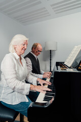 Older couple studying piano together and reading music sheet