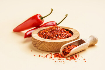 Wooden bowl of chipotle chili flakes on color background