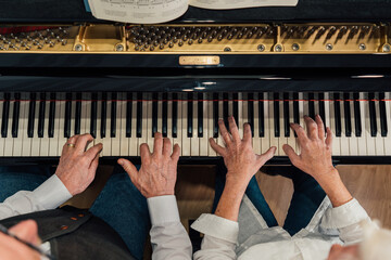 Overhead view of four hands from older couple playing a grand piano