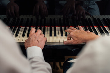 Close-up view of four hands from older couple playing a grand piano