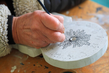 mano de persona mayor pintando con un pincel una flor en un reloj eguzkilore país vasco...