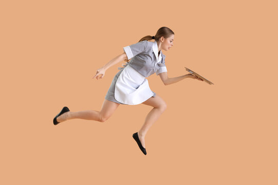 Young waitress with tray jumping on beige background