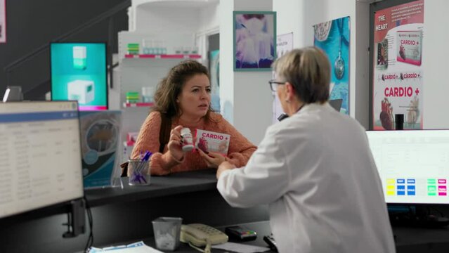Female client asking specialist about cardiology pills in boxes and bottles, talking about vitamins and medicine at cash register desk. Customer buying pharmaceutics drugs at drugstore counter.