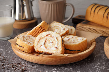 Wooden plate with pieces of delicious sponge cake roll on table